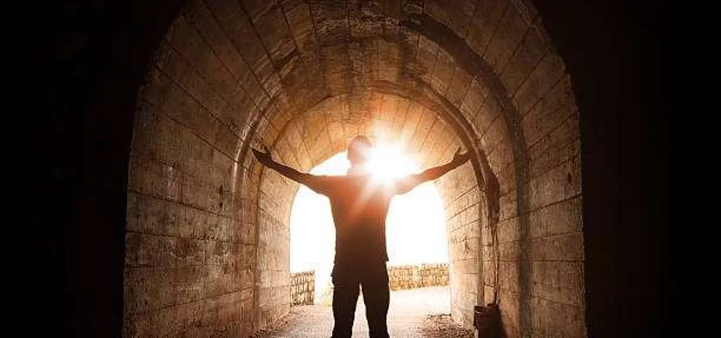 Man stands inside of old dark tunnel with shining sun in the end